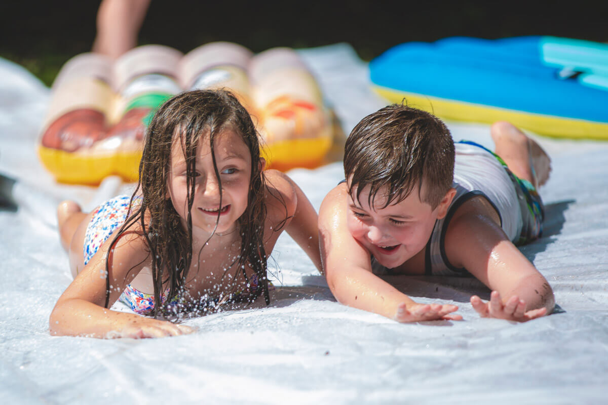 Two 6 year old children slidding belly down on a slip and slide