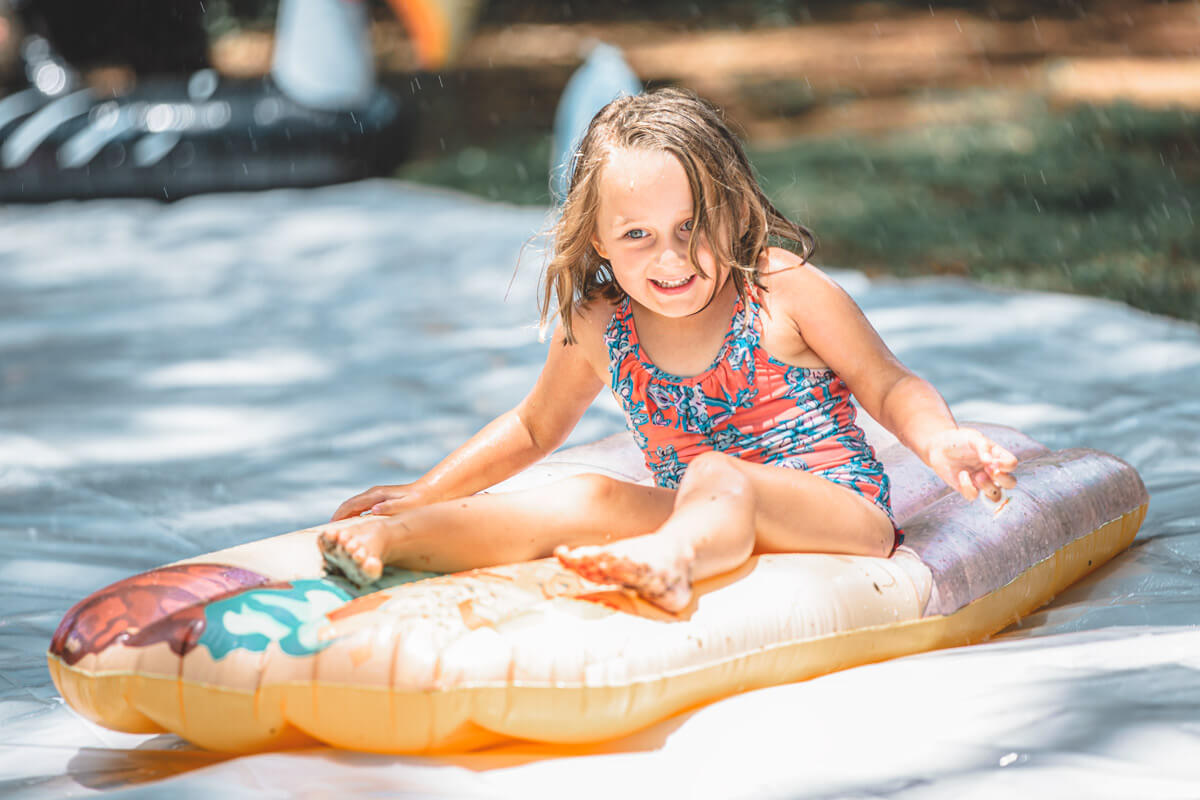 six year old on a pool raft slides down slip and slide