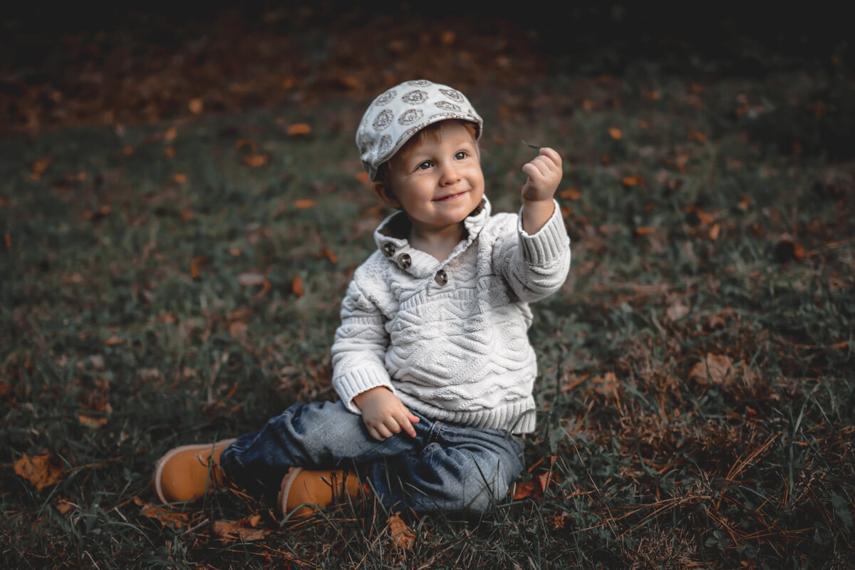 Color enriched photo of a child sitting on grass and holding up a single blade of grass